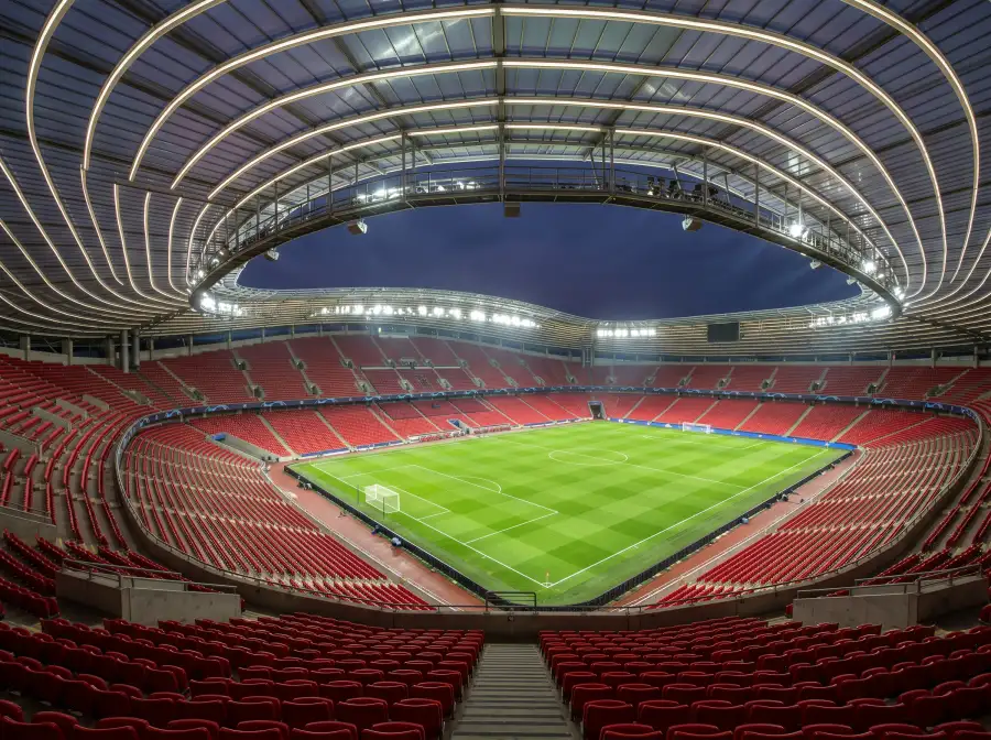 Estadio de futbol moderno con techo curvado y cesped impecable visto desde una grada alta
